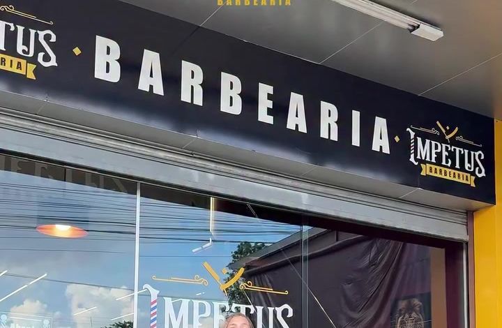 Fachada da Impetus Barbearia, com o letreiro preto sobre a vitrine de vidro